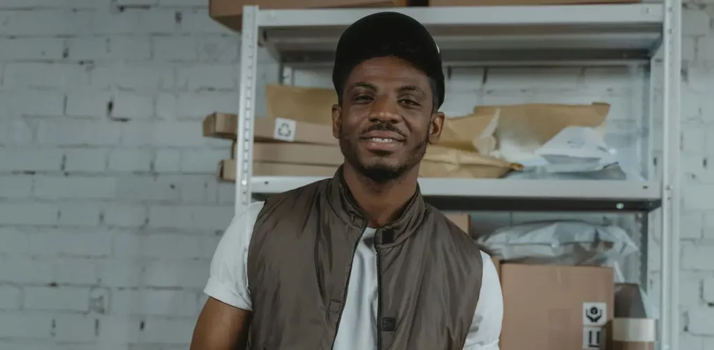 A Man Smiles While Holding A Clipboard In A Spacious Warehouse Environment