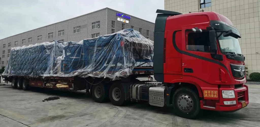 A Large Truck Carrying A Sizable Container On Its Back, Parked On A Street With Clear Blue Skies In The Background