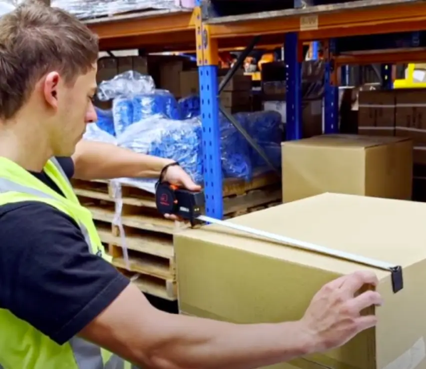 A Man Measures Boxes With A Tape Measure, Focusing On The Dimensions For Organization Or Packing Purposes